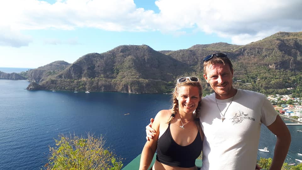 Laura y Neil sonríen a cámara con el mar y las montañas detrás